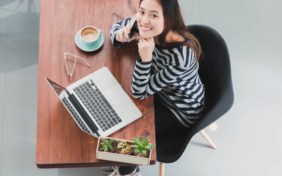 Young beautiful Asian woman working and talking with smart phone and laptop in coffee shop background with copy space.Concept of female freelancer.Vintage tone